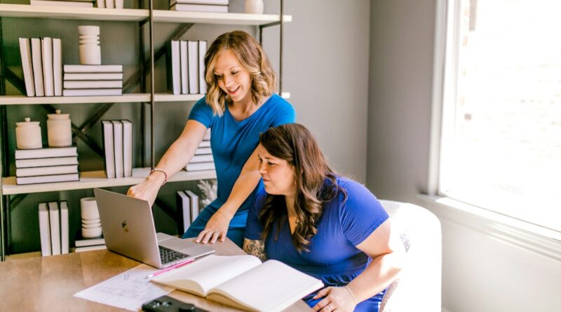 Two colleagues reviewing a notebook beside a laptop