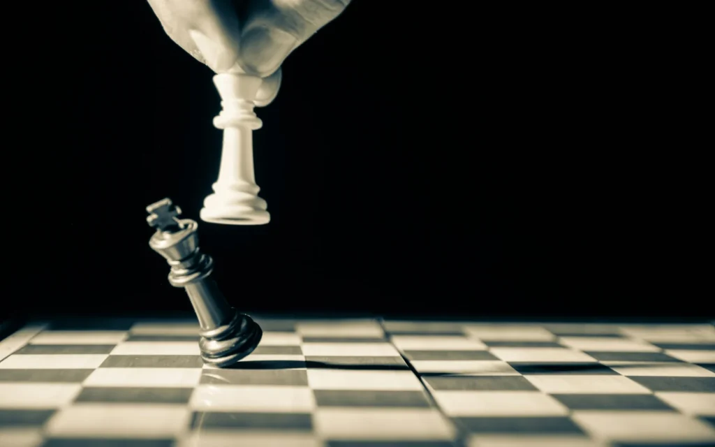 A hand moving a white chess piece beside a tilted black king