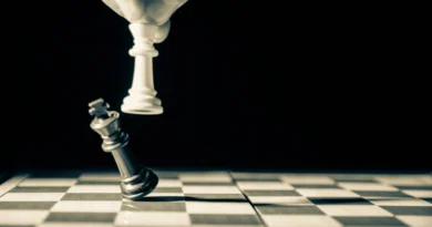 A hand moving a white chess piece beside a tilted black king