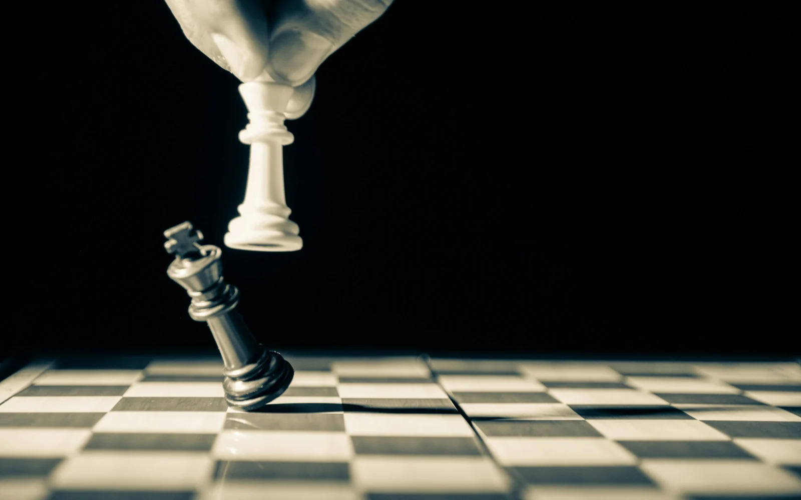 A hand moving a white chess piece beside a tilted black king
