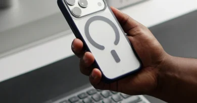 A hand holding a smartphone beside a desktop computer and keyboard
